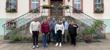 7 Frauen und Männer stehen vor einer Eingangstreppe